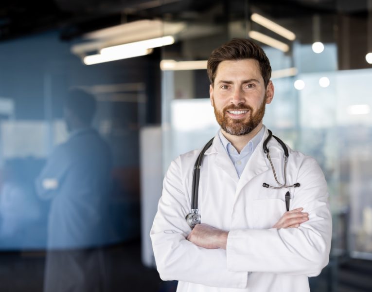 Smiling,Male,Doctor,With,Stethoscope,In,Professional,Hospital,Setting.,Confident