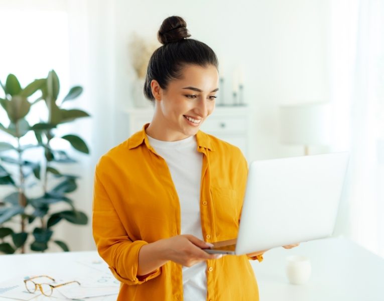 Confident woman holding a laptop in a bright workspace, representing the benefits of Answer Engine Optimization services for modern businesses.