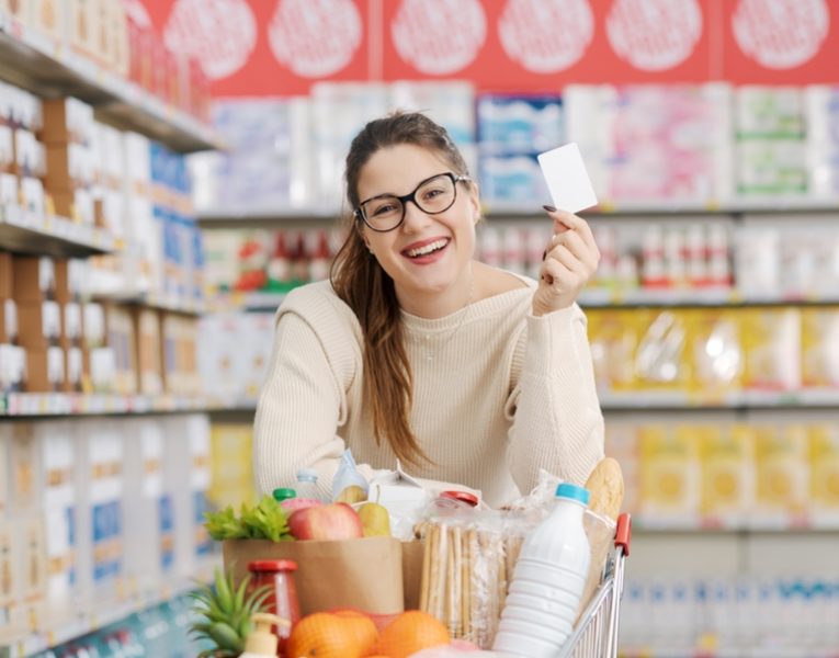 Smiling,Customer,Leaning,On,A,Full,Shopping,Cart,And,Showing